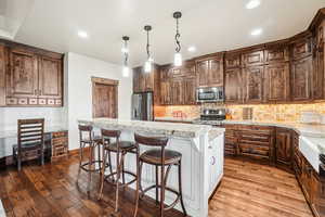 Kitchen with appliances with stainless steel finishes, dark wood-style flooring, tasteful backsplash, a center island, and a kitchen bar