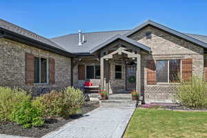 Property entrance with brick siding, covered porch, a shingled roof, and a yard