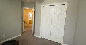 Unfurnished bedroom featuring dark carpet, baseboards, and a closet