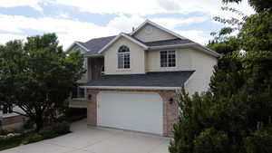 Traditional-style house featuring concrete driveway, an attached garage, brick siding, stucco siding, and roof with shingles