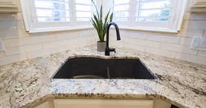 Kitchen view of a sink, backsplash, light stone countertops, and white cabinets