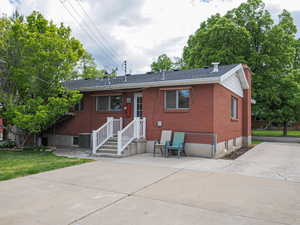Single story home with brick siding, central air condition unit, a patio, a chimney, and a shingled roof