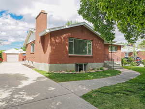 View of property exterior with a chimney, an outdoor structure, concrete driveway, a yard, and brick siding