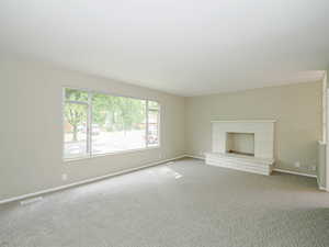 Unfurnished living room featuring carpet flooring, baseboards, and a brick fireplace