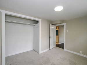 Unfurnished bedroom featuring light colored carpet, a closet, and baseboards