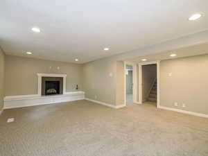 Unfurnished living room featuring stairway, light colored carpet, recessed lighting, a fireplace with raised hearth, and baseboards