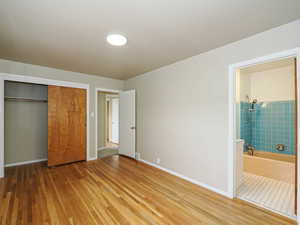 Unfurnished bedroom featuring wood finished floors, a closet, baseboards, and ensuite bathroom