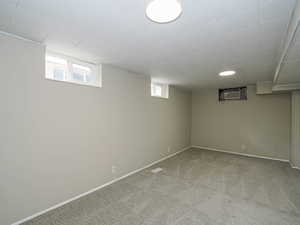 Basement featuring carpet flooring, healthy amount of natural light, a wall mounted AC, and baseboards