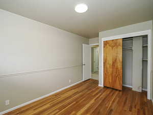 Unfurnished bedroom featuring wood finished floors, a closet, and baseboards
