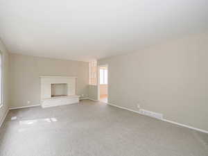 Unfurnished living room featuring carpet, a fireplace with raised hearth, and baseboards