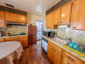 Kitchen featuring under cabinet range hood, black electric stovetop, a sink, dark wood-style flooring, and stainless steel microwave