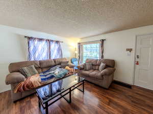 Living area featuring dark wood-type flooring, a textured ceiling, and baseboards