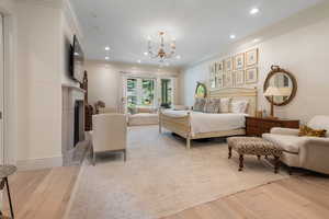Bedroom with wood finished floors, ornamental molding, a chandelier, a fireplace, and recessed lighting