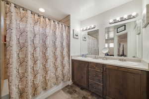 Bathroom with shower / bath combination with curtain, double vanity, and stone finish floors