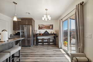 Kitchen with stainless steel fridge with ice dispenser, a sink, a chandelier, light wood-type flooring, and hanging light fixtures