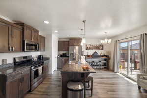 Kitchen with stainless steel appliances, a sink, dark wood finished floors, a chandelier, and dark stone countertops