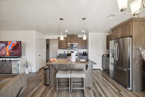 Kitchen with stainless steel appliances, light wood-type flooring, dark stone countertops, a breakfast bar, and a sink