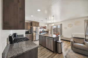 Kitchen featuring stainless steel appliances, a sink, open floor plan, light wood finished floors, and dark brown cabinetry
