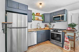 Kitchen with appliances with stainless steel finishes, a sink, decorative backsplash, and light wood-style flooring
