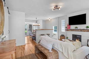 Living area with a chandelier, light wood-style flooring, a glass covered fireplace, and baseboards