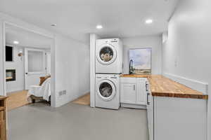 Washroom with stacked washing machine and dryer, cabinet space, a glass covered fireplace, baseboards, and recessed lighting