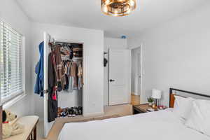 Bedroom with multiple windows, light colored carpet, baseboards, and a closet