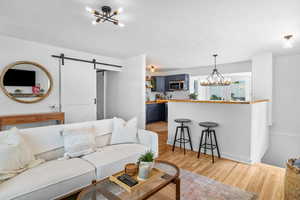 Living room featuring a chandelier, a barn door, light wood-style flooring, and baseboards