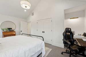 Carpeted bedroom with high vaulted ceiling, a desk, and a closet