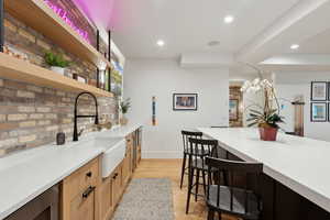 Kitchen featuring open shelves, a sink, a kitchen breakfast bar, baseboards, and recessed lighting