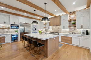 Kitchen with open shelves, beverage cooler, stainless steel appliances, backsplash, and a breakfast bar area