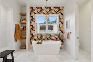 Full bathroom featuring a freestanding tub, toilet, marble finish floors, baseboards, and a chandelier