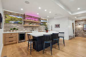 Indoor wet bar featuring beverage cooler, brick wall, light wood-style floors, recessed lighting, and baseboards