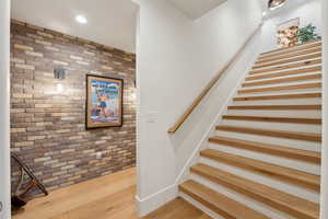 Stairs featuring brick wall, wood finished floors, and recessed lighting