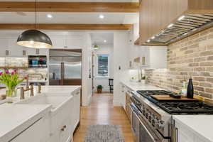 Kitchen with high quality appliances, wall chimney exhaust hood, white cabinetry, light wood-type flooring, and tasteful backsplash