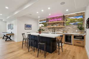 Indoor wet bar with beverage cooler, light wood-style floors, recessed lighting, stainless steel microwave, and baseboards