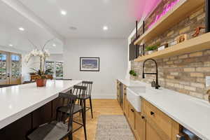Kitchen with a sink, light countertops, recessed lighting, open shelves, and a breakfast bar area