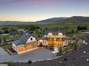 Back of property at dusk featuring a mountain view, covered porch, concrete driveway, and stone siding