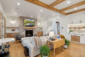 Living area with light wood-style flooring, recessed lighting, beamed ceiling, and a brick fireplace