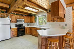 Kitchen with freestanding refrigerator, black / electric stove, stainless steel microwave, wooden ceiling, and brown cabinetry