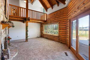 Unfurnished living room featuring log walls, plenty of natural light, carpet flooring, high vaulted ceiling, and beam ceiling
