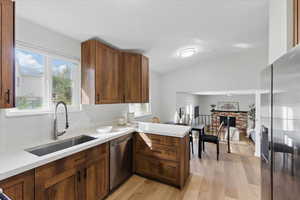 Kitchen with appliances with stainless steel finishes, a sink, a peninsula, light countertops, and lofted ceiling