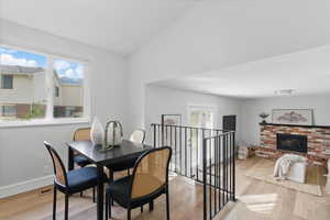 Dining room with light wood-type flooring, plenty of natural light, a fireplace, baseboards, and vaulted ceiling