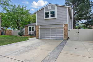 View of front of home featuring a gate, driveway, brick siding, and an attached garage