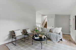Living room with stairs, light wood-style flooring, and baseboards