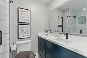 Full bathroom featuring tiled shower, toilet, vanity, and baseboards