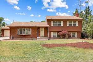 Tri-level home with a chimney, a garage, a front yard, concrete driveway, and brick siding