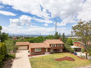 Split level home featuring driveway, a garage, a front lawn, a chimney, and brick siding
