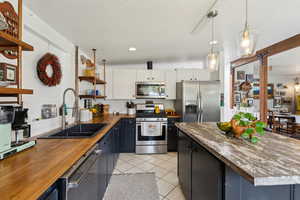 Kitchen featuring appliances with stainless steel finishes, wood counters, a sink, open shelves, and light tile patterned floors