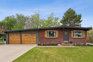 View of front of house featuring concrete driveway, a front lawn, brick siding, and a garage