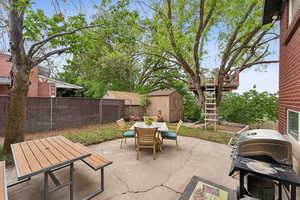 View of patio with outdoor dining area, a storage unit, a fenced backyard, an outdoor structure, and stairway